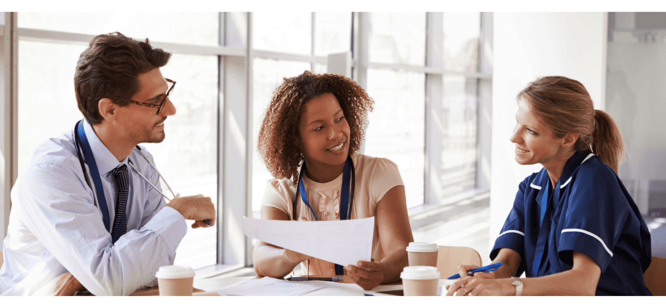 Drie zorgprofessionals in overleg aan tafel met documenten en koffie